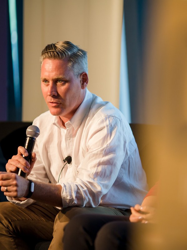 Mark Cameron in conversation, holding a microphone during a panel session